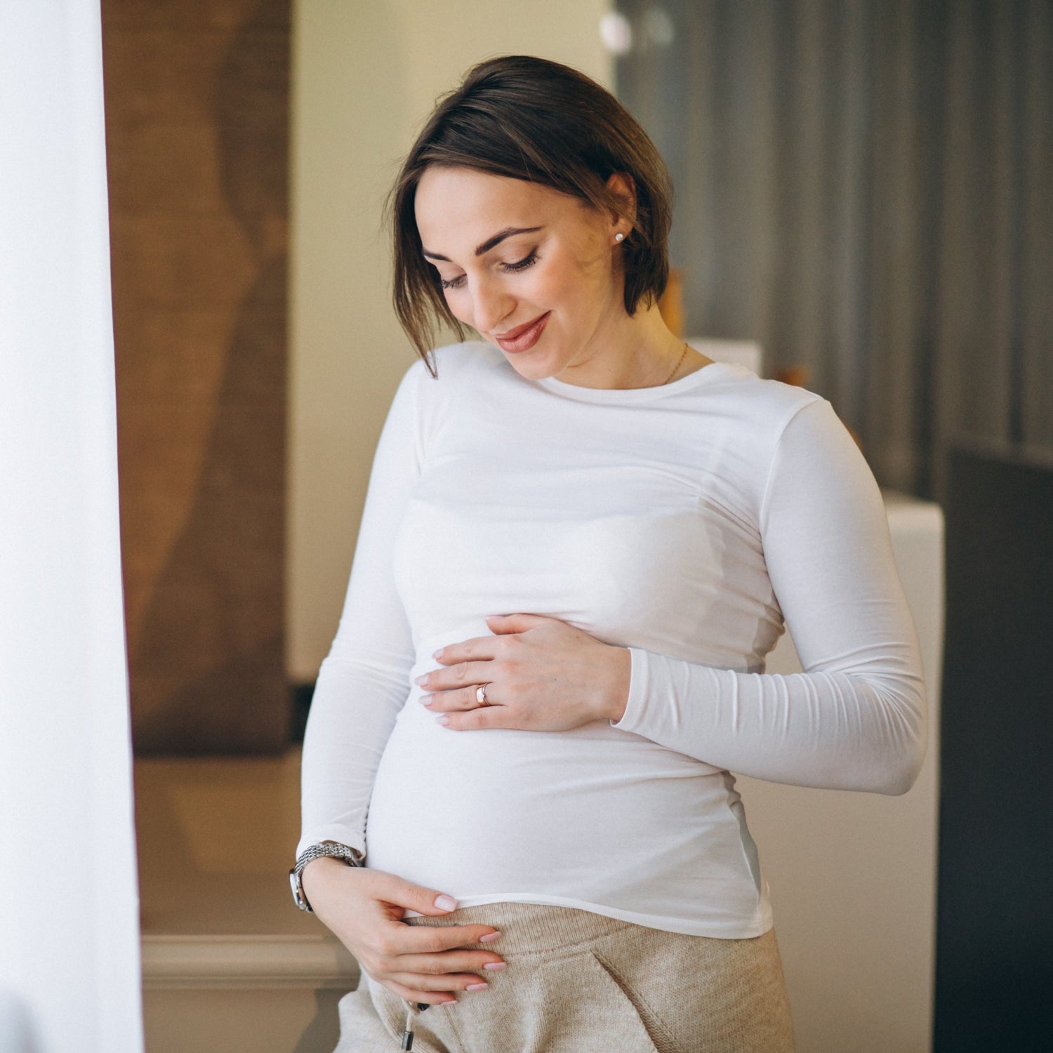 joven embarazada de pie junto la ventana en casa portada TPNI casos especiales PLUS